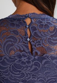 Spetsblus med detaljerade blommönster i djup marinblått, med knäppning bak och scallopkrage.