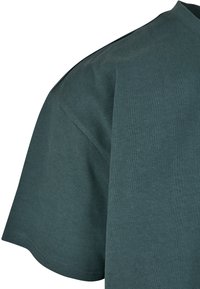 T-shirt à manches courtes en bleu sarcelle foncé, fabriqué en coton doux. Présente un col rond et une coupe décontractée avec un tissu texturé.
