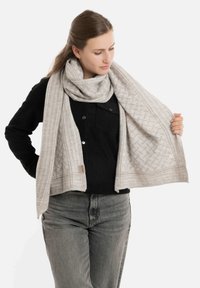 Lichtgrijze sjaal met een geometrisch patroon, gemaakt van zacht materiaal, met een gestructureerde afwerking en een merktab aan de rand.