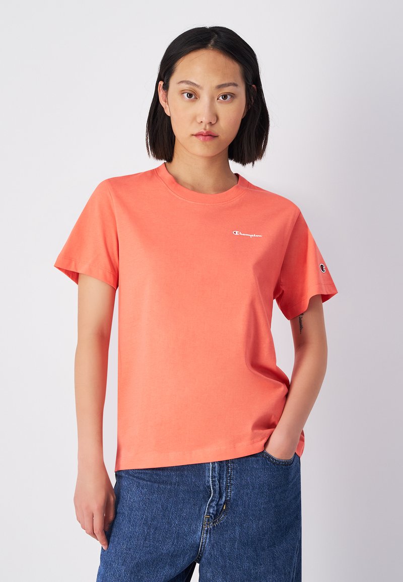 Koraalrood katoenen T-shirt met korte mouwen, ronde halslijn, logo op de borst, gecombineerd met hoogrisp blauwe denim jeans.