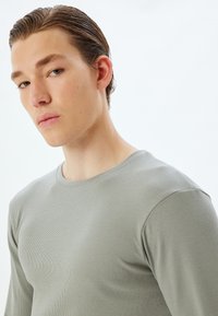 Lichtgrijs langemouwen shirt met een ribbelstructuur en ronde hals, snug fit rond de schouders en de borst.
