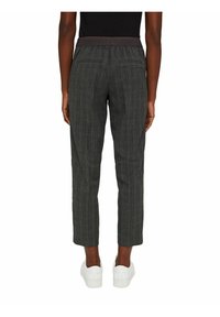 Personne portant un pantalon court gris à carreaux avec une ceinture élastique noire et des baskets blanches, vue de dos sur un fond blanc.