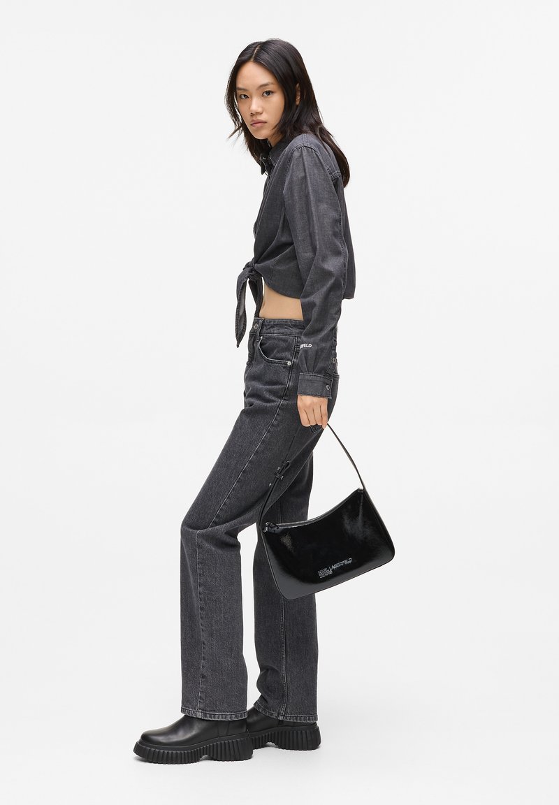 Svart cropped denimskjorta med knyt framtill, grå flare-jeans, svarta klackboots och en glänsande svart handväska. Slät textur, minimal detaljer.