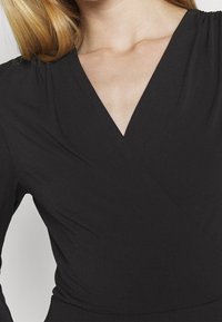 Černé zavinovací šaty s V výstřihem, vyrobené z hladkého materiálu. Mají na ramenou nařasené detaily a přiléhavý siluetu.