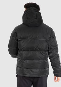 Sort polstret jakke med hætte, der har et quiltet design, frontsømmene og en glat, blank overflade. Velegnet til kolde vejrforhold.