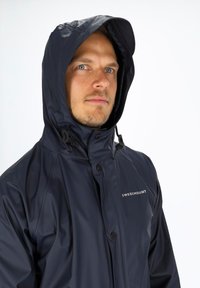 Marineblauer wasserdichter Jacke mit hohem Kragen und Kapuze, mit einem vorderen Knopfverschluss und dem Logo "SWEDEMOUNT" auf der Brust.