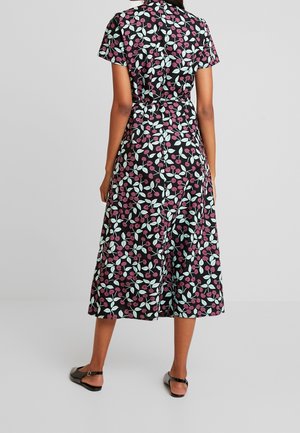 Robe fleurie noire à manches courtes, ornée de baies roses et de feuilles vertes. Mi-longue, coupe décontractée, avec une taille cintrée et des détails à boutons.