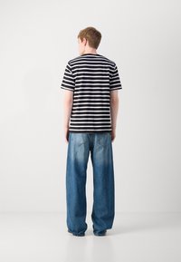 Black and white striped short-sleeve t-shirt paired with loose, faded blue denim jeans, featuring large pockets and a relaxed fit.