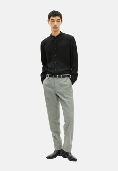 Chemise noire à manches longues avec une texture subtile, associée à un pantalon à carreaux gris. Une ceinture noire et des chaussures en cuir noir complètent la tenue.