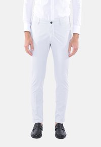 Pantaloni slim-fit grigio chiaro realizzati in tessuto morbido. Presentano una chiusura frontale con bottone e tasche laterali. Indossati con scarpe nere.