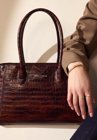 Brown crocodile-embossed leather handbag with two rounded handles, featuring gold branding on the front and a structured silhouette.