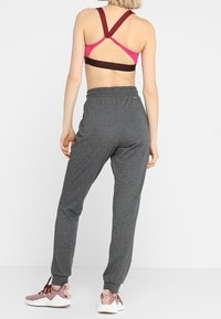 Conjunto deportivo que incluye un sujetador deportivo de tirantes en burdeos y rosa, y pantalones deportivos grises con cinturilla elástica y puños en los tobillos.