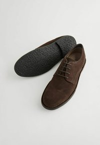Zapatos de vestir de ante marrón con punta redonda y diseño de cordones. Suela de goma negra texturizada. Forro interior suave.