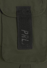 Grüner Stoffklappe mit einem schwarzen gewebten Riemen, der schwach sichtbaren, teilweise sichtbaren silbernen Text zeigt.