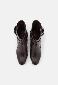 Un par de botas de tobillo marrón oscuro con un patrón texturizado y hebillas laterales, vistas desde arriba sobre un fondo blanco.