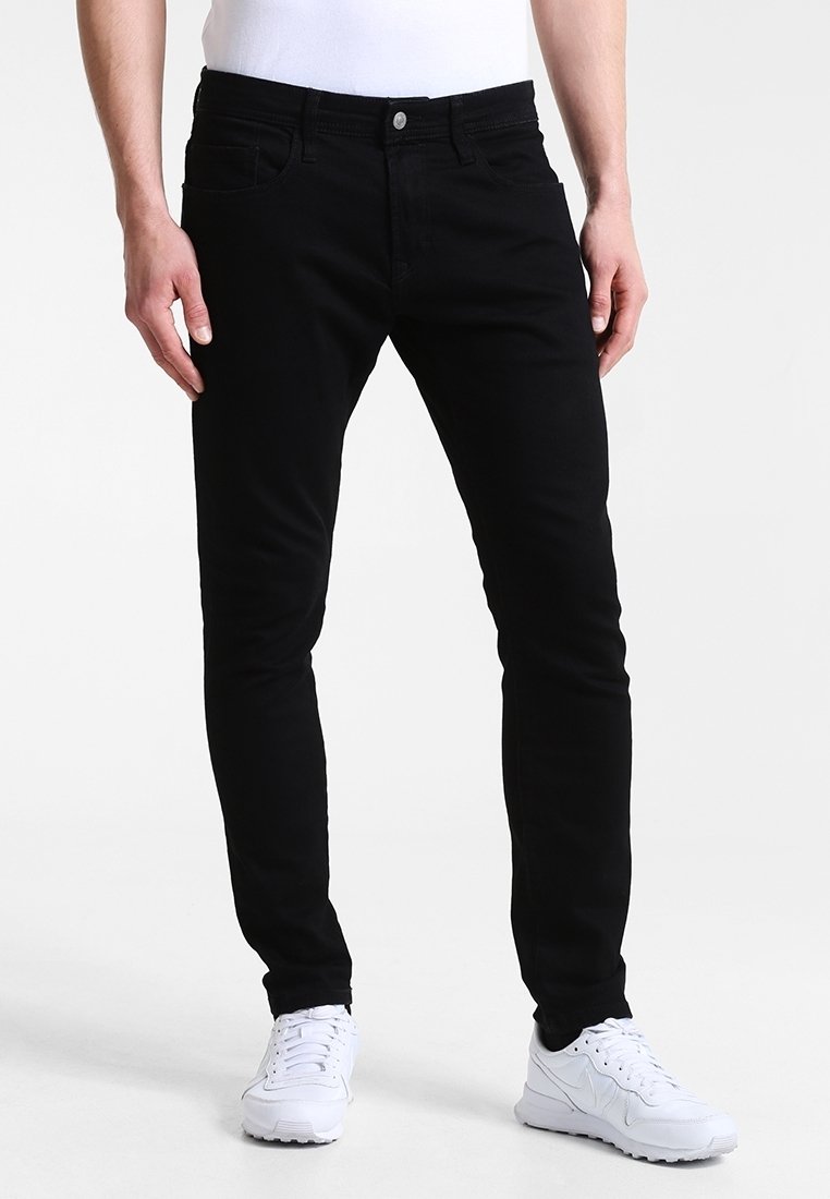 Jean noir slim-fit avec cinq poches, en denim, doté d'une fermeture à boutons et de passants pour ceinture. Associé à des baskets blanches.