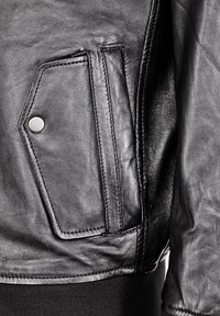 Svart läderjacka med en texturerad yta, med en snedställd ficka och tryckknappdetalj. Nederkanten är av solid kvalitet, vilket ökar hållbarheten.