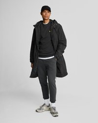 Black parka with a hood, layered over a black sweatshirt and gray joggers. Gray sneakers with white accents and a black cap.
