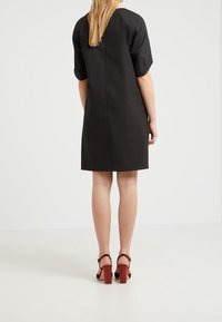 Schwarzes kurzes Kleid mit gerader Silhouette, knielangem Saum und glatter Textur. Kombiniert mit roten High-Heels.