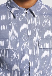 Blue and white patterned shirt with a zip closure, collared design, textured fabric, and two front pockets.