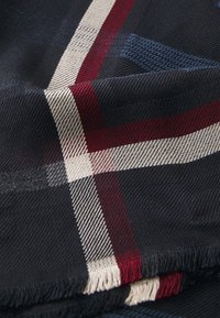 Laivastonsininen huivi, jossa on ruudullinen kuvio, jossa on valkoisia, punaisia ja sinisiä yksityiskohtia. Hapsutettu reuna ja teksturoitu kangas.