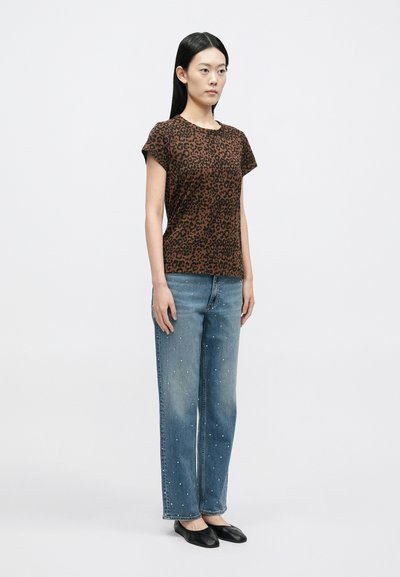 Καφέ τοπ με κοντά μανίκια σε σχέδιο λεοπάρ, συνδυασμένο με ανοιχτό μπλε τζιν με λευκές διακοσμήσεις. Μαύρα μπαλαρίνες ολοκληρώνουν την εμφάνιση.