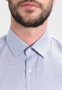 Ljusblå skjorta med knappar i en strukturerad tyg, med en formad krage och två vita knappar på knappsl ån.