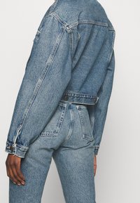 Ljust blå denimjacka med avslappnad passform, med sidoknappar och sömdetaljer. Matchad med ljusblå jeans.