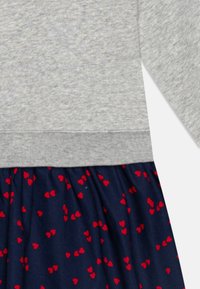 Grå övre del med en texturerad yta, som övergår till en marinblå kjol med spridda röda hjärtan. Blandad tyg med elastiskt kant.