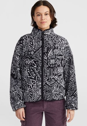Zwart-witte fleecejack met abstracte geometrische patronen, hoge kraag, hetelangerits en een ritszak op de borst. Zachte textuur.
