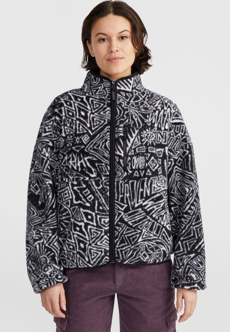 Veste polaire noire et blanche avec des motifs géométriques abstraits, col montant, fermeture éclair à l'avant et poche poitrine zippée. Texture douce.