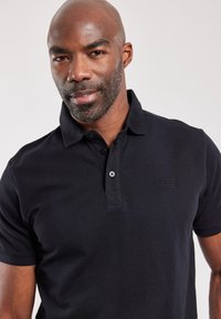 Zwarte polo met een gestructureerde stof, drie knopen en een subtiel logo op de borst, met een klassieke kraagontwerp.