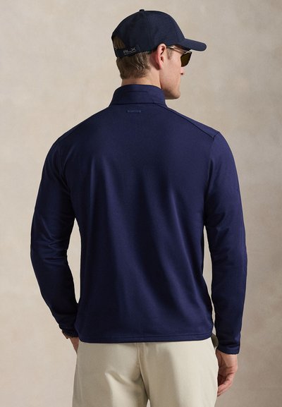 Μπλε σκούρο πόλο μακρυμάνικο με γιακά, με λεία, υφή υφάσματος. Διαθέτει διακοσμητικά στους ώμους και ετικέτα της μάρκας στον αυχένα πίσω.