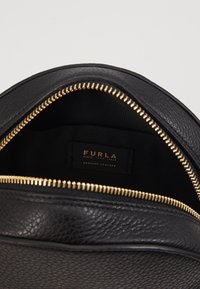 Zaino in pelle nera con superficie texturizzata, dettagli in zip dorata e interno in tessuto. Etichetta visibile: "FURLA, Pelle Vera."