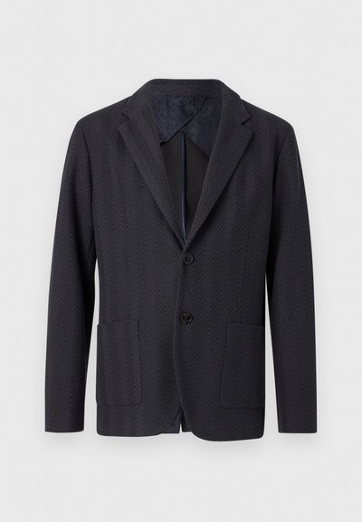 Blazer en chevrons bleu marine avec deux poches avant, fermeture par un seul bouton, col à cran, et doublure intérieure contrastante. Tissu texturé.