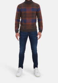 Hnědý a modrý kostkovaný svetr s rolákem a žebrovaným lemem, kombinovaný s tmavě modrými slim-fit džíny a bílými teniskami.