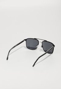 Ochelari de soare negri cu lentile pătrate, sticlă gri colorată, accente argintii subțiri pe ramă și brațe din plastic negru.