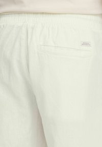 Lichtkleurige linnen broek met een elastische tailleband, een achterzak en een label met de tekst "Toegewijd aan Denim Perfectie."