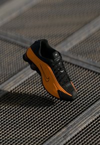 Sapatilha Nike com um cabedal preto e realces laranja vibrantes, sola de borracha texturizada e elementos de design streamlined.