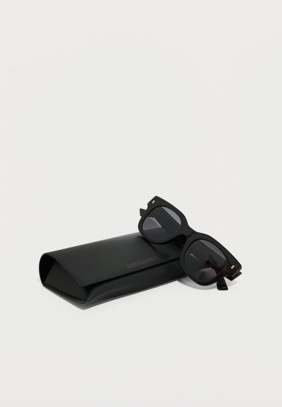 Γυαλιά ηλίου με μαύρο τετράγωνο πλαίσιο, ακουμπισμένα επάνω σε μια μαύρη ορθογώνια θήκη με διακριτικό ανάγλυφο λογότυπο της μάρκας.