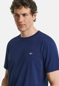 Navyblauwe katoenen t-shirt met een ronde halslijn en korte mouwen. Voorzien van een klein geborduurd logo op de borst. Gladde textuur.