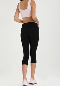 Czarne legginsy capri z wysokim stanem, zestawione z jasnoróżowym topem bez rękawów z perforowanymi detalami na plecach.