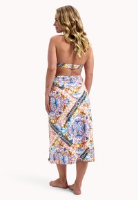 Top sin tirantes con una cinta estampada, combinado con una falda larga floral en tonos rosas, azules y dorados, con un diseño envolvente.