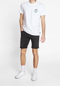 Bílý bavlněný tričko s kulatým výstřihem a kruhovou grafikou "Hawaii". V kombinaci s černými džíny a bílými teniskami.