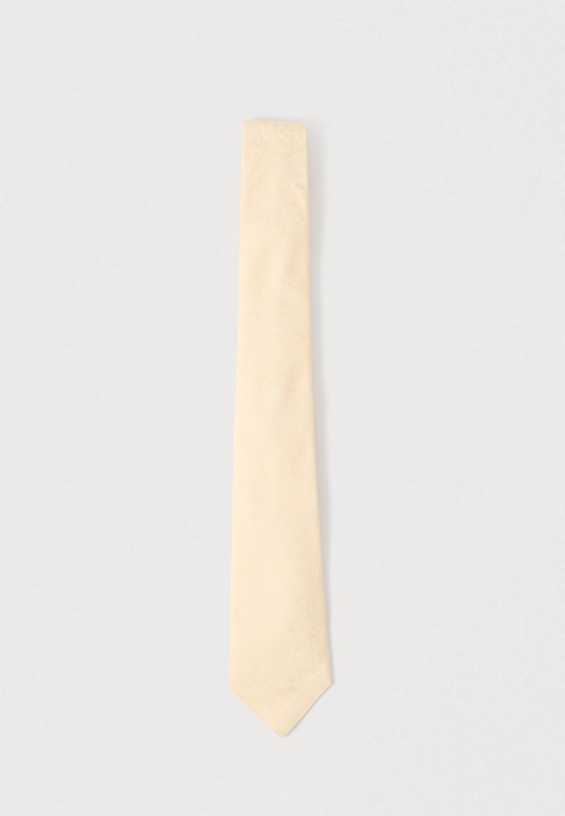 Krémově zbarvená kravata s jemným květinovým žakárovým vzorem, úzký střih a špičatý konec na jednobarevném světle šedém pozadí.