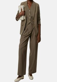 Hnědý pruhovaný oblek s upraveným sakem a širokými kalhotami. Obsahuje vestičku s knoflíky a světle béžovou kabelku. Texturované mokasíny.