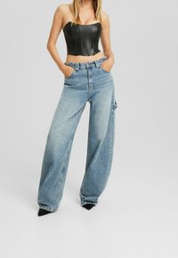 Černý kožený cropped top s vertikálními švy, spárovaný s světle modrými širokými džínami s bočními kapsami a vysokým pasem. Černé špičaté lodičky.