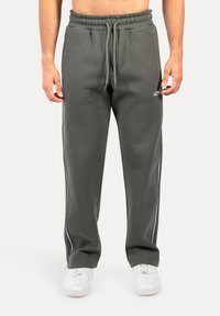 Dunkelgrüne Trainingshose mit einem Kordelzugbund, seitlichen Streifen und weichem Material, kombiniert mit weißen Turnschuhen.