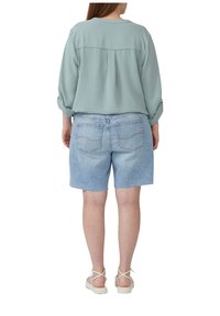 Hellgrüne, strukturierte Bluse mit Rundhalsausschnitt, kombiniert mit hellblauen Denim-Shorts mit fransigem Saum und Gesäßtaschen.