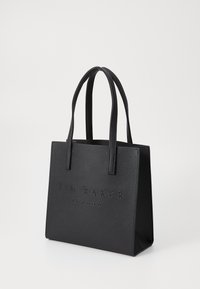 Sac fourre-tout noir en matériau synthétique texturé, avec un logo en relief sur le devant, des poignées duales et une forme rectangulaire structurée.